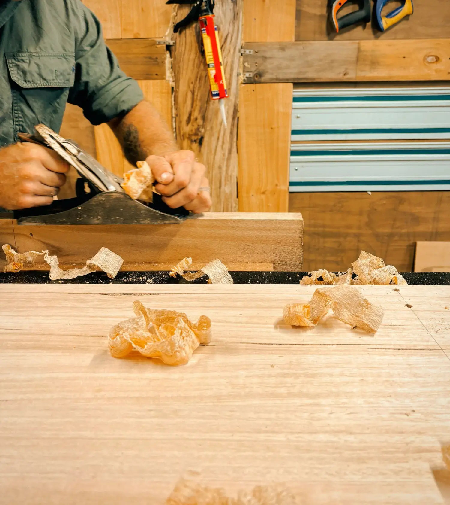 Hands carving a small timber piece with shavings on the workbench
